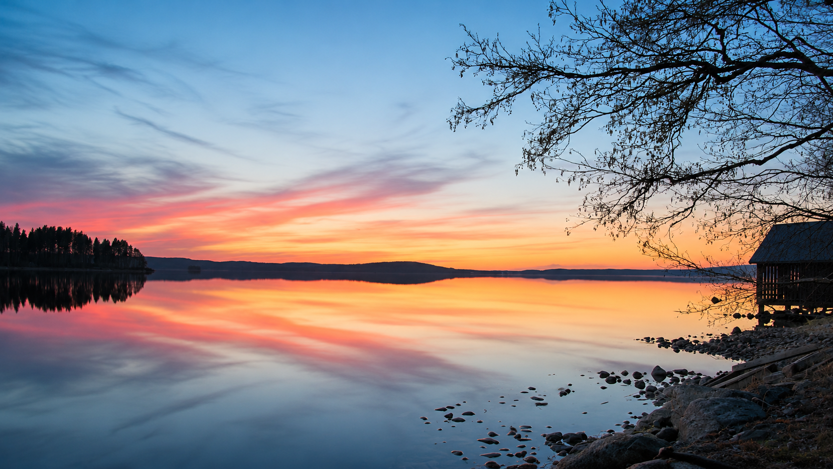 Auringonlaskun värit heijastuvat tyynestä järvestä Luhangan rantamaisemassa.